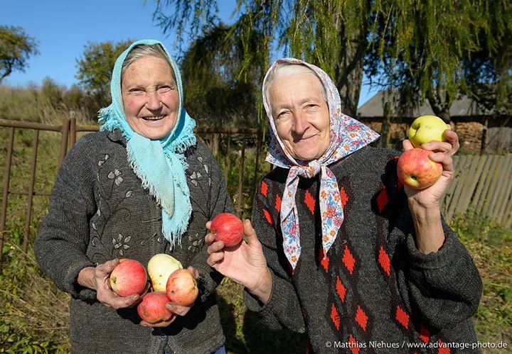 Zwei ältere Damen stehen in einem Garten und halten Apfel in der Hand.