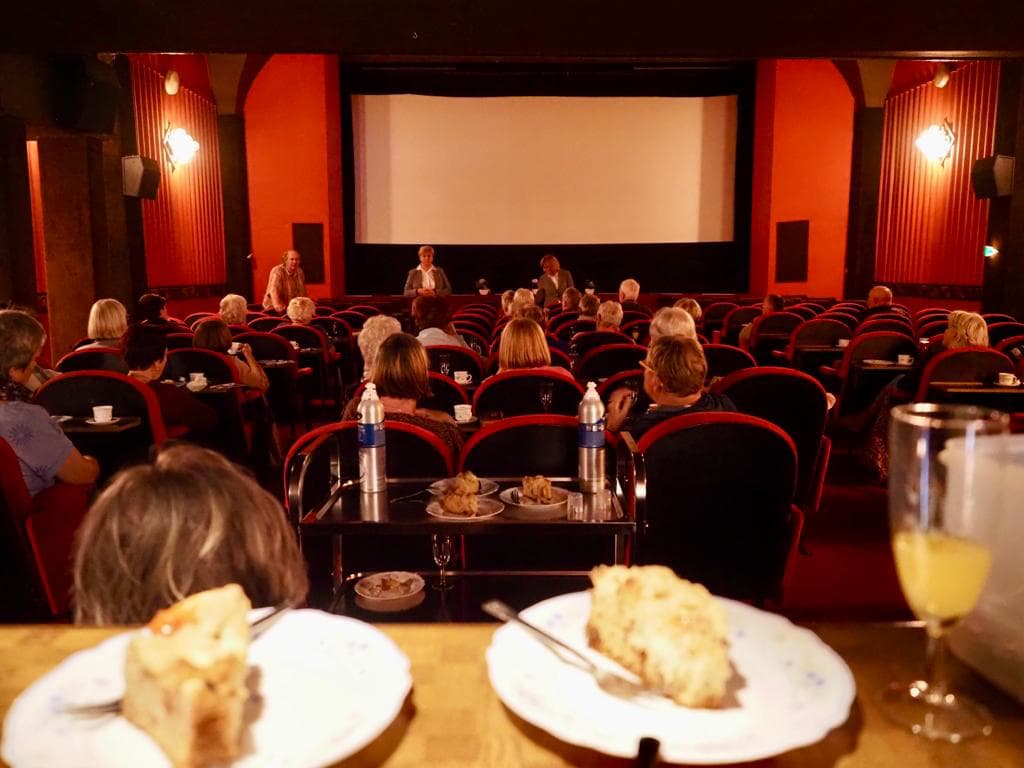 Film-Cafe Malteser Lohne Ein abgedunkelter Kinosaal mit älteren Besuchern. Eine Helferin reicht einem Besucher Kaffee.