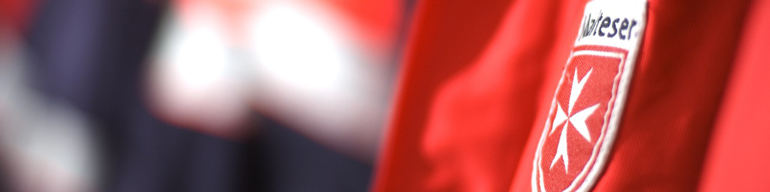 Das Logo der Malteser als Aufnäher auf einer roten Malteser-Jacke.
