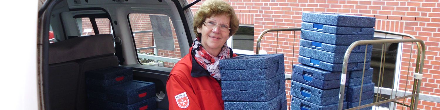 Eine ältere Dame hält mehrere blaue Styrophorboxen mit Essen in der Hand.