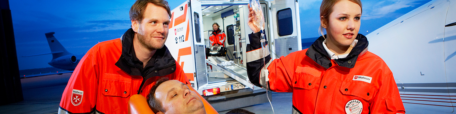 Zwei Rettungssanitäter fahren einen Patienten auf einer Trage zum Rettungswagen.